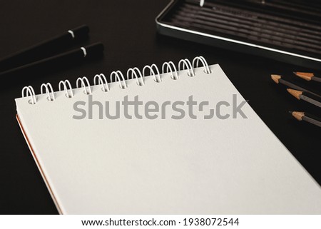 Blank notepad with white sheets on a dark table closeup. Writing diagonal mockup great for adding any drawing. Glasses and pencils in a background. Small focal length.