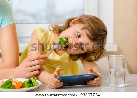 The problem is to distract the child from the phone and feed it with broccoli. Organic food and vegetables on a plate. A way to feed children