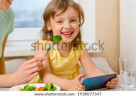 A happy child eats broccoli only with cartoons. Organic cabbage and food on a plate. The problem of feeding the children preschool age