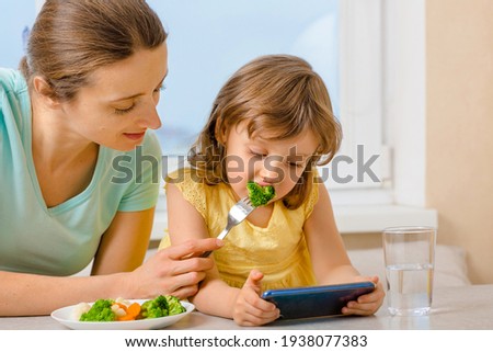 Mom and her daughter show Dad how great they eat broccoli, via videoconference. Eating organic food. A way to feed children