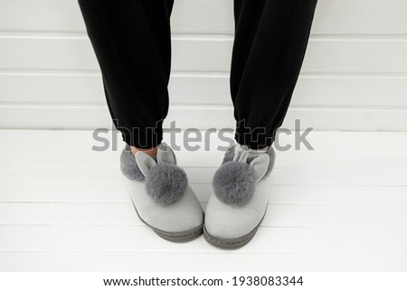 Beautiful fur slippers with ribbons in a shape of a rabbit put on women legs standing on a white background