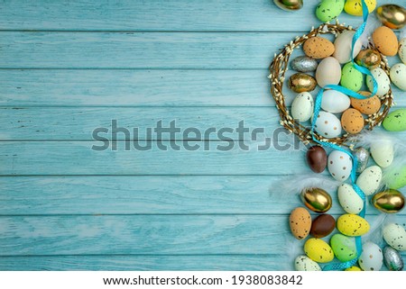 Chocolate eggs with a satin ribbon surrounded by sweet treats colorful candies. A wreath of twigs. Light blue wooden background and copy space. Modern greeting card for the celebration of Easter.