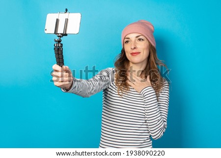 Young woman blogger takes pictures of himself on the phone on a blue background. Concept story, vlog, selfie, blog.