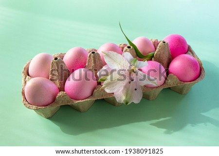 Minimal Easter concept. Festive spring mood, natural decor. Easter elements, paper box with eggs in pink colors and flower on pastel green background. 