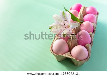 Minimal Easter concept. Festive spring mood, natural decor. Easter elements, paper box with eggs in pink colors and flower on pastel green background. Copy space.