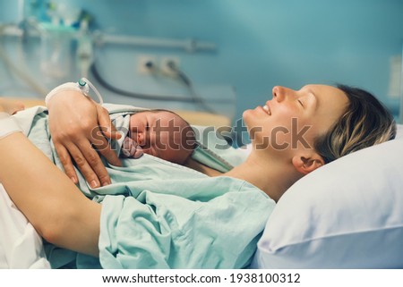 Mother and newborn. Child birth in maternity hospital. Young mom hugging her newborn baby after delivery. Woman giving birth. First moments of baby life after labor. Royalty-Free Stock Photo #1938100312