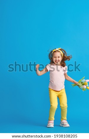 charming little girl with curly hair and headband with bouquet colorful tulips made fabric jumps to her full height on blue background studio. Dynamic image. concept of spring and Easter.