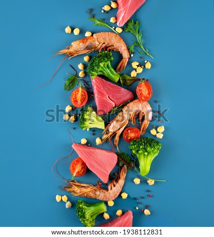 Shrimp, tuna, broccoli, cherry tomatoes and chickpea on a bright blue background. Concept Healthy Pescatarian diet. Seafood, fish, vegetables.Pescetarian and Flexsitarian diet plan products.Top view Royalty-Free Stock Photo #1938112831