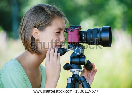 Young charming calm woman in a green blouse takes pictures on a red camera with a large lens in the summer park. Royalty-Free Stock Photo #1938119677