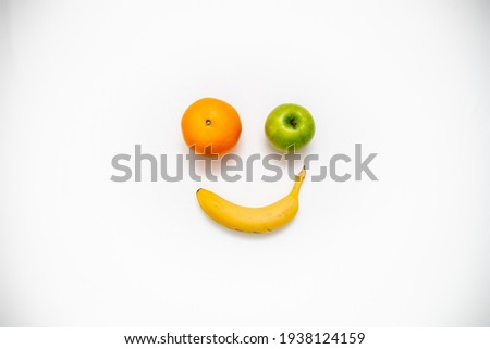 Smiley face made out of fruits on white background. Banana orange and green apple on a picture.