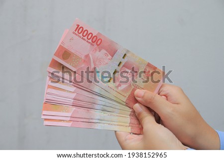woman's hand showing rupiah banknotes on white background. IDR 100000. Royalty-Free Stock Photo #1938152965