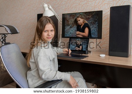 a girl is sitting at a computer table in her apartment and is editing her image using a graphics tablet