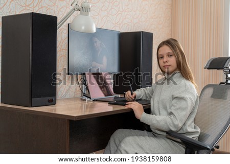 a girl is sitting at a computer table in her apartment and is editing her image using a graphics tablet