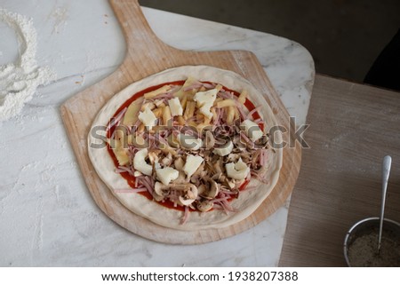 A pizza with ingredients on wooden paddle