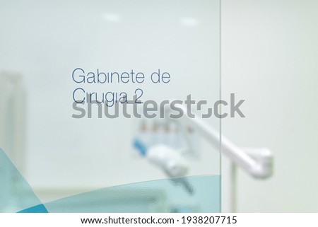 Sign on glass door reading "gabinete de cirugía 2" in Spanish with operating apparatus in background
