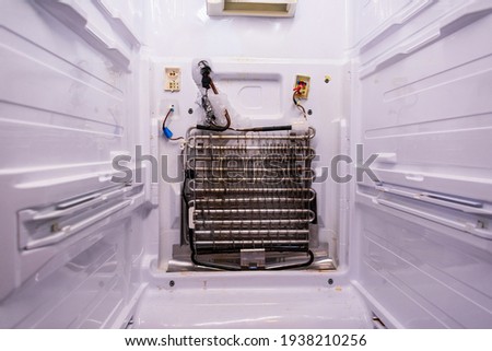 Refrigerator repair. Freezer compartment back panel removed. Evaporator coils with a frozen thermostat Royalty-Free Stock Photo #1938210256