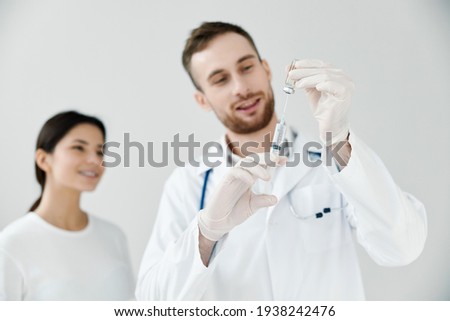 happy doctor holding syringe with covid-19 vaccine and female patient in the background