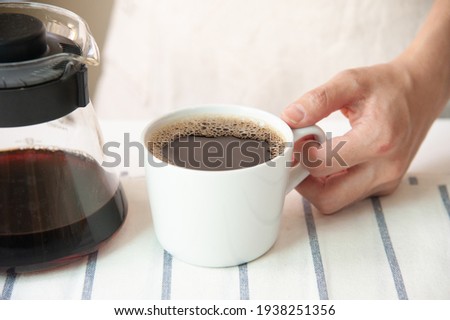 Crop of barista holding cup of coffee with jug at home