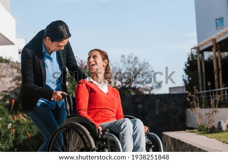 Happy young latin woman in wheelchair and her friend having fun outdoors in Mexico Royalty-Free Stock Photo #1938251848