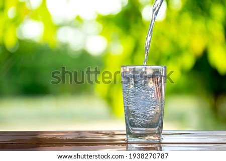 Water flows into a glass placed on a wooden bar. Royalty-Free Stock Photo #1938270787