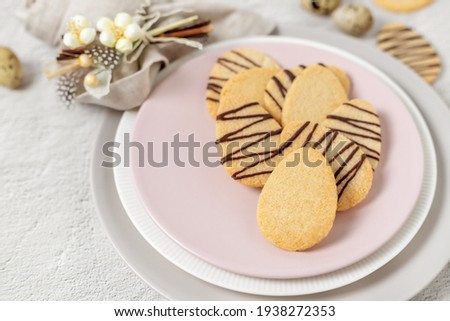 Easter shortbread cookies, home baked egg shaped biscuits on a pink round plate, sweet treats rustic table place setting arrangement on a stone surface and spring flowers