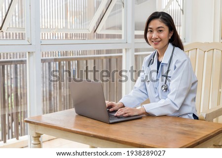 Female doctor working with laptop in modern private hospital.Selective focus with blur background.Woman with white medical gown suit typing on notebook at clinic corridor.Nice and beautiful smile.