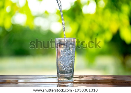 Water flows into a glass placed on a wooden bar. Royalty-Free Stock Photo #1938301318