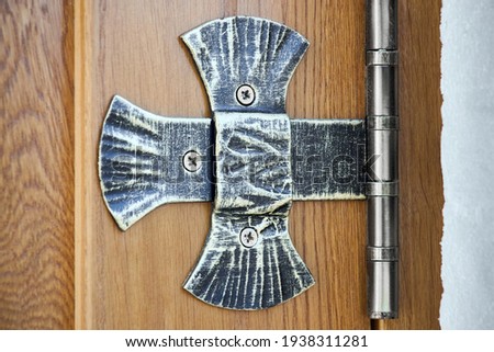 Forged aged patinated cross-shaped ornamented door hinge on wooden vintage church door.