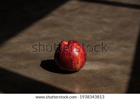 A red apple in dark and light structure background in natural light in an artistic way.
