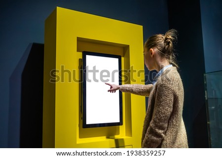 Woman hand using vertical white blank interactive touchscreen display of electronic multimedia kiosk in dark room - scrolling and touching. Mock up, copyspace, template and technology concept Royalty-Free Stock Photo #1938359257