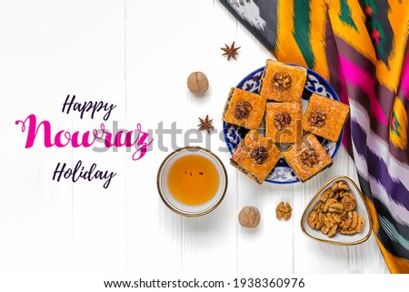 Traditional arabic dessert baklava with walnuts, raisins on plate, bowl, teapot with Uzbek national ornament on white wooden table Text Happy Nowruz Holiday Concept of spring came Top view Flat lay