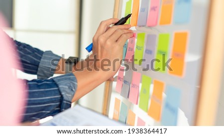 man is writing by the right hand on notepapers that stick on white board. wears stripped blue shirt. hands and notepapers. Royalty-Free Stock Photo #1938364417