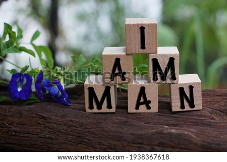 Wooden block with words I AM MAN on nature background.
