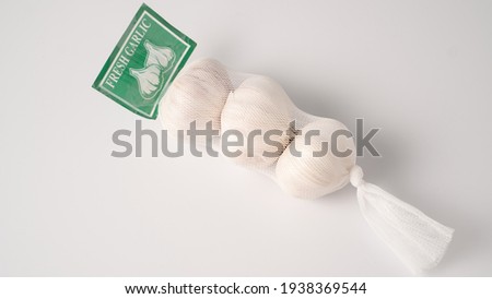 Garlic in net. Garlic packaging nets. Three garlic heads packaged in a mesh bag. Fresh garlic head wrapped in mesh bag Royalty-Free Stock Photo #1938369544
