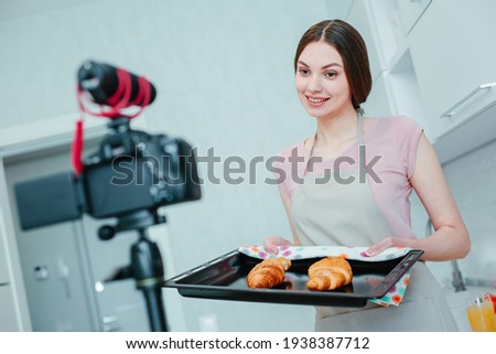 Cheerful young woman with fresh pastry on a baking pan smiling to the camera in the kitchen Royalty-Free Stock Photo #1938387712