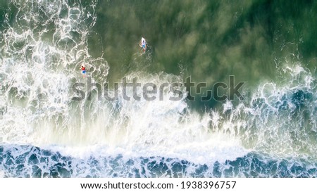 Aerial photo of ocean beach landscape in Tel Aviv, Israel showing a lone surfer paddling over a swell in green mediterranean waters on their surfboard with waves and white water crashing around them 