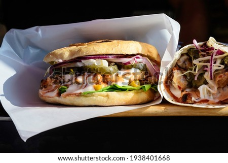 Close up of a tasty hamburger or burger sandwich, with grilled spiced meat with mayonnaise, pickled cucumbers, red onion and green salad, displayed for sale at a street food market, selective focus
