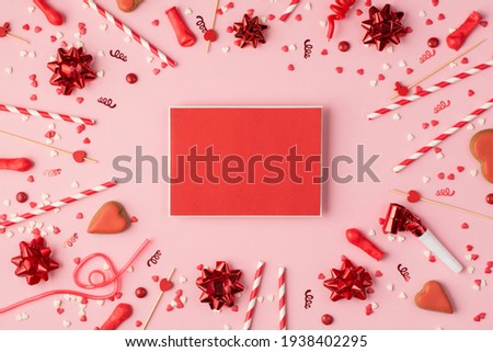 Top view photo of birthday composition with red ribbon stars serpentine confetti heart-shaped cookies bright decorations red empty card template in the middle on pastel pink background with copyspace
