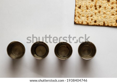 Matzah - Jewish bread for Passover. Next to four silver cups. White background