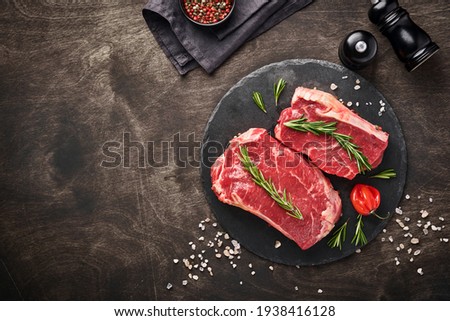 Two raw steak New York  with rosemary and spices on a piece of parchment paper on old dark stone background. Top view. Mock up. Royalty-Free Stock Photo #1938416128