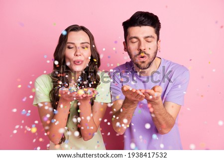 Portrait of attractive dreamy cheerful couple blowing decorative elements isolated over pink pastel color background