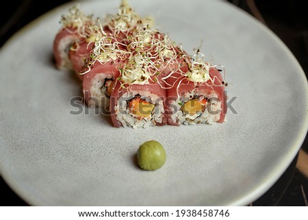Set of delicious sushi rolls decorated with sprouts served on white plate with wasabi on black background. Healthy gourmet raw cuisine. Food photography, restaurant service concept