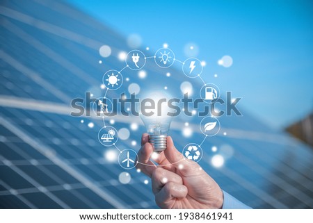 The man holds a light bulb, LED bulb on a background of solar panels with icons energy sources for renewable, sustainable development. Ecology concept