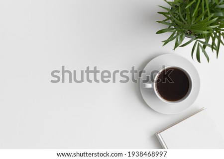 Workspace accessories, cup of coffee and a palm on the white table. Flat lay with blank copy space. Royalty-Free Stock Photo #1938468997