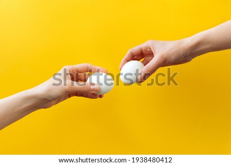 Woman hands holding Easter eggs for knocking on yellow background. Easter celebration or creative concept. Adam creation Royalty-Free Stock Photo #1938480412