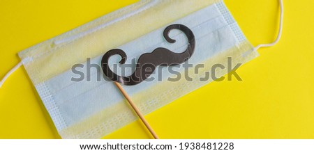 Medical face mask, paper black mustache on a stick on bright yellow background, close-up. Celebrating April Fools ' Day during the coronavirus pandemic.