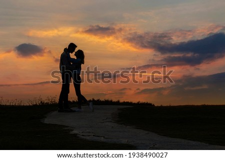 Couple in love kissing at sunset. Silhouette of two people on a background of beautiful evening sky. Royalty-Free Stock Photo #1938490027