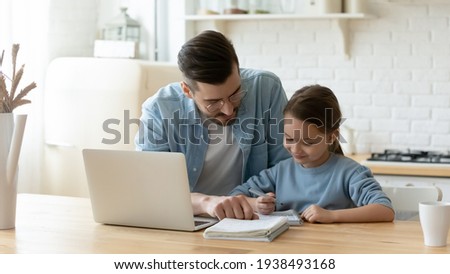 Caring young dad helping small primary pupil kid daughter preparing school homework, sitting together at table. Happy little child girl involved in doing task, studying homeschooling with father. Royalty-Free Stock Photo #1938493168