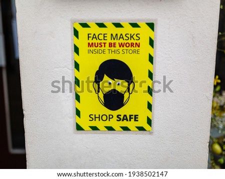 A wall sign stating that face masks must be worn while inside the store. Comedy googly eyes have been stuck on the eyes