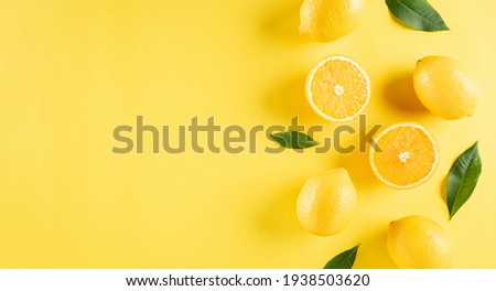 Summer composition made from oranges, lemon and green leaves on pastel yellow background. Fruit minimal concept. Flat lay, top view, copy space.